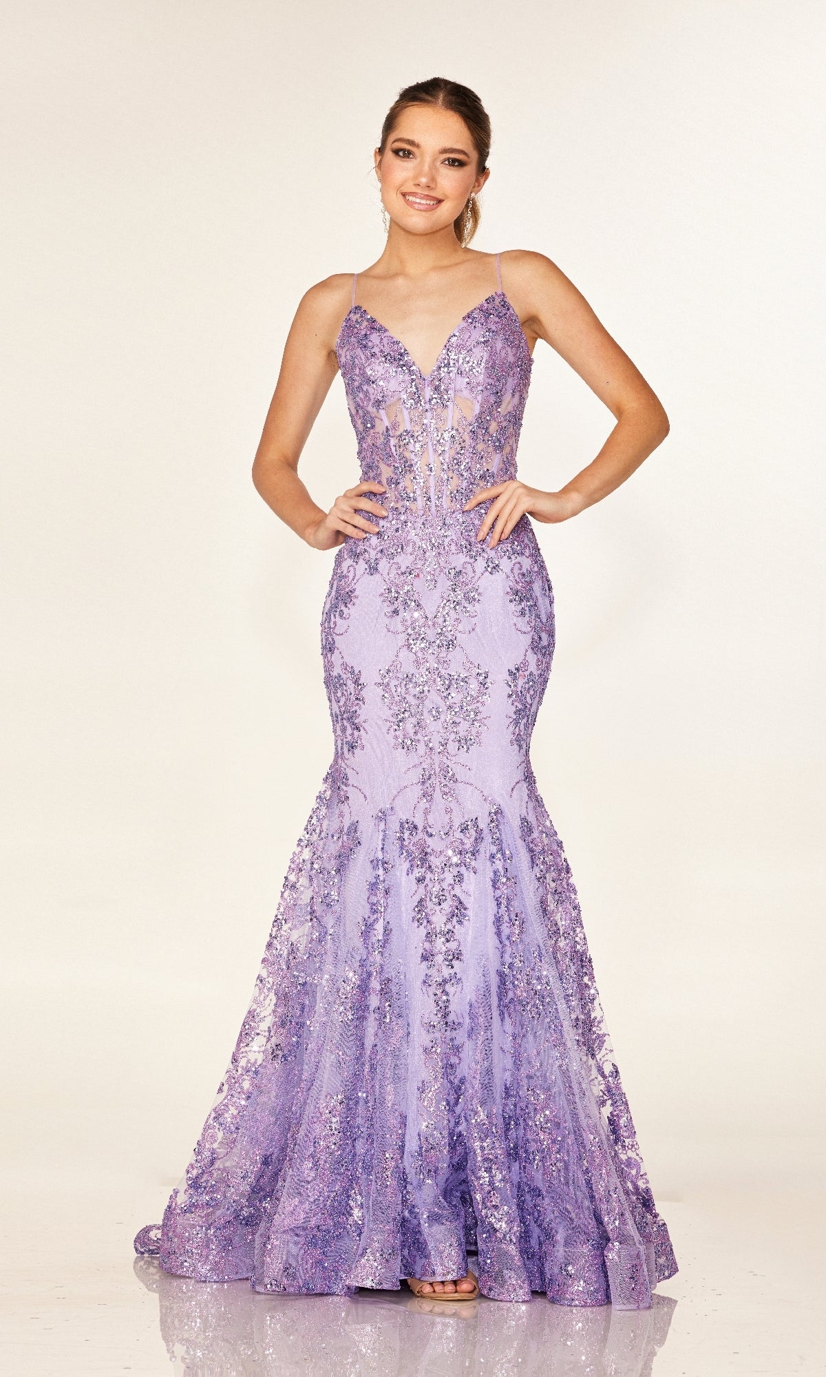 A woman poses with hands on hips in the Cecilia Couture 2641 long prom dress, a fitted, floor-length lavender mermaid gown with thin straps and floral sequin embellishments, set against a plain backdrop.